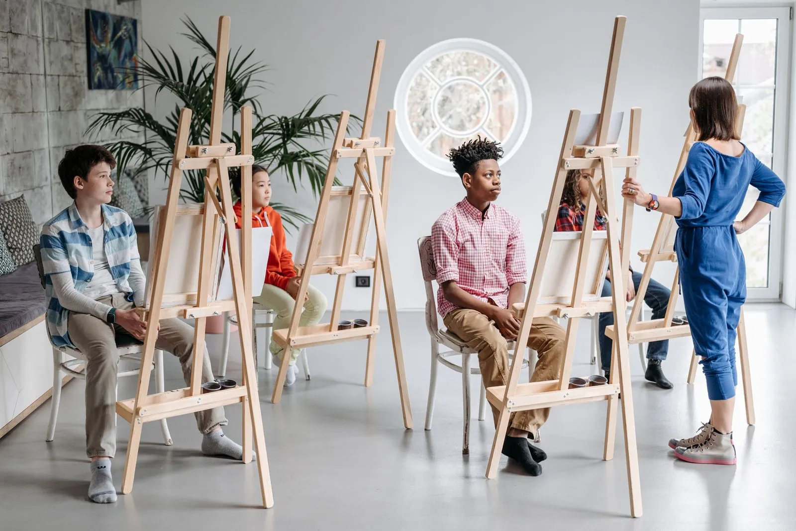 Children in an art class, guided by a teacher, engaging in creativity with easels.